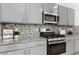 Close-up showcasing the kitchen's gray cabinetry, mosaic backsplash, granite countertops, and stainless steel appliances at 5317 Golden Melody Ln, North Las Vegas, NV 89081