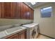 Well-equipped laundry room with modern washer, dryer, sink, and wooden storage cabinets at 11573 Glowing Sunset Ln, Las Vegas, NV 89135