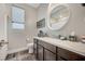 Bathroom with dark cabinets, white counters, a round mirror and a window at 5479 Tamar Ridge Ct, Las Vegas, NV 89141