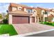 View of a two-story townhome, showcasing the paved driveway, two car garage and landscaping at 5492 Royal Vista Ln, Las Vegas, NV 89149