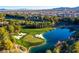 Aerial view of golf course with a picturesque pond, lush green fairways, sand bunkers, and houses in the distance at 21 Grand Masters Dr, Las Vegas, NV 89141
