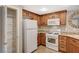 Compact kitchen featuring wooden cabinets, granite countertops, white appliances, and a pantry at 50 Aura De Blanco St # 19103, Henderson, NV 89074