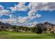 Scenic view of a lush green golf course with mountain backdrop under a bright blue sky with scattered clouds at 3116 Richland Dr, Las Vegas, NV 89134