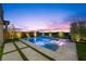 A luxurious pool with in-pool loungers is beautifully lit at dusk, surrounded by manicured landscaping at 298 Watteau Ct, Henderson, NV 89012