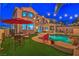 Backyard with outdoor dining set, lush artificial grass, and a beautifully illuminated swimming pool with rock features at 2749 Carolina Blue Ave, Henderson, NV 89052