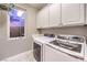 Functional laundry room equipped with side-by-side washer and dryer, and white storage cabinets at 47 Strada Principale, Henderson, NV 89011