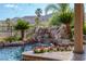 Close-up of a waterfall cascading into a blue lagoon-style pool, surrounded by lush greenery and rock features at 11359 Winter Cottage Pl, Las Vegas, NV 89135