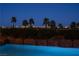 Inviting backyard pool and rock feature with palm trees and a stunning city skyline view at night at 5020 Spanish Heights Dr, Las Vegas, NV 89148