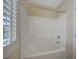 Well-lit white tiled bathtub and shower combo with window featuring shutters, offering modern comfort at 7822 Whitlocks Mill Ave, Las Vegas, NV 89147