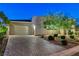 Well-lit home exterior with brick driveway and manicured landscaping at dusk at 10004 Terrastone Dr, Las Vegas, NV 89148