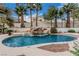 Backyard pool with rock waterfall feature, tiled spa, and rock landscaping surrounded by palm trees at 227 Drysdale Cir, Henderson, NV 89074