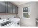 Laundry room featuring gray cabinets, modern washer and dryer, granite countertop, and a bright window at 292 Crimson Edge St, Henderson, NV 89012