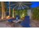 Outdoor lounge chairs under an umbrella surrounded by lush landscaping with lighting at 8808 Rozetta Ct, Las Vegas, NV 89134