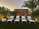 A lovely backyard with four white lounge chairs, decorative side tables and mature landscaping at 6316 Bluejay Way, Las Vegas, NV 89146