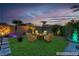 Outdoor living area with modern seating, lush landscaping, and vibrant uplighting at dusk at 9091 Becket Ranch Ct, Las Vegas, NV 89113