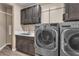A laundry room with dark cabinets, solid surface countertop, stainless steel sink, and stainless steel front load washer and dryer at 9091 Becket Ranch Ct, Las Vegas, NV 89113
