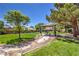 Inviting common area featuring covered picnic tables, barbecue grills, lush greenery, and mature trees under a clear blue sky at 8942 Galena Crossing St, Las Vegas, NV 89123
