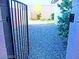 A peek through a backyard gate at the gravel and lush green landscaping at 95 Palm Park Ct, Las Vegas, NV 89183