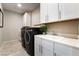 Bright laundry room featuring a utility sink, shaker cabinets, and modern, front-loading washer and dryer at 10313 Jade Point Dr, Las Vegas, NV 89135