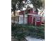 Charming exterior view of the red, two-story home with a lattice-enclosed porch and mature trees at 1385 Ringe Ln, Las Vegas, NV 89110