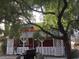 Front exterior view of the red home featuring a porch with lattice, framed by a large tree at 1385 Ringe Ln, Las Vegas, NV 89110