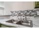 Close-up of a stainless steel kitchen sink, marble countertops, mosaic backsplash, and olive green cabinetry at 1400 Jamielinn Ln # 104, Las Vegas, NV 89110