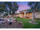 Lush backyard featuring a covered patio, rock waterfall, vibrant green grass, and mature trees at twilight at 1234 Campbell Dr, Las Vegas, NV 89102