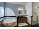 Stylish bathroom featuring soaking tub, decorative half-moon window, tiled half wall, and vanity with granite countertop at 6236 Desert Haven Rd, Las Vegas, NV 89130