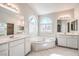 Light and bright bathroom featuring dual vanities, a soaking tub under arched windows, and tile flooring at 1563 Cattle Ranch Pl, Henderson, NV 89002
