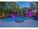 Backyard pool and spa illuminated with blue and purple lights surrounded by lush trees and landscaping at 1925 Grey Eagle St, Henderson, NV 89074