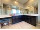 Bathroom with double sinks, tiled floors, large mirrors, and dark cabinets with white countertops at 10152 Tenaya Meadows St, Las Vegas, NV 89178