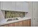 Modern laundry room featuring white cabinets and a stainless steel sink with green tile backsplash at 10528 Garden Light Dr, Las Vegas, NV 89135