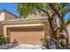 Beige two-story home with a large two-car garage, complemented by mature trees at 9773 Bedstraw St, Las Vegas, NV 89178