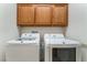 Bright laundry room with side-by-side appliances, wooden cabinets for storage, and white walls at 9812 Turtle Walk Ave, Las Vegas, NV 89149