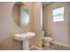 Stylish powder room with pedestal sink, oval mirror, toilet, and a window providing natural light at 3636 Chelsea Gardens Dr, Las Vegas, NV 89135