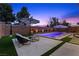 Backyard pool with tanning ledge, patio and artificial turf, with lounge seating and shade umbrellas, at dusk at 940 Viscanio Pl, Las Vegas, NV 89138