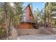 A-frame cabin surrounded by mature trees, with a brick foundation and staircase leading to a spacious deck at 2160 Via Vita St, Mount Charleston, NV 89124