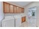 Well-equipped laundry room with wooden cabinets, washer, dryer, sink, and view into kitchen at 2377 Baldwinville Ct, Henderson, NV 89044