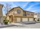 Exterior view of a three-story townhome with garages, beige stucco, and manicured landscaping at 6255 W Arby Ave # 118, Las Vegas, NV 89118