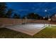 Night view of a backyard sports court featuring basketball hoops and a net with a brick wall and grass at 7360 Dolphine Crest Ave, Las Vegas, NV 89129