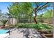 Landscaped backyard featuring mature shade trees, green grass, privacy fence, and a quaint patio area at 1861 Windward Ct, Henderson, NV 89012