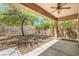 Covered patio with a large shade tree overlooking the fenced-in gravel yard and hillside at 35 Glade Water Dr, Henderson, NV 89052