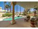 This backyard features a patio with columns that overlooks a luxurious pool area with a waterfall and palm trees at 8838 Spanish Mountain Dr, Las Vegas, NV 89148