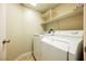 This laundry room includes a white washer and dryer with shelving above for storage at 10404 Shadowland Ave, Las Vegas, NV 89144