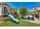 Backyard view of a playhouse with a slide, lush landscaping, and a covered patio by the swimming pool at 13 Cozy Glen Cir, Henderson, NV 89074