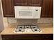 Granite countertops surround a cooktop, with wood cabinetry and a built-in microwave above at 3004 Darby Falls Dr, Las Vegas, NV 89134