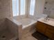 Bright bathroom featuring a soaking tub, marble tile surround, and a wooden vanity at 7313 Bosky Springs St, Las Vegas, NV 89131
