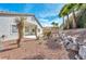 View of home's backyard with desert landscaping and rock retaining wall with palm trees in background at 129 Sapodilla Ln, Las Vegas, NV 89144