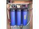 Water filtration system showcasing three large blue filters, plumbing, and various supplies mounted on a wooden frame at 3708 Calumet Farm Cir, North Las Vegas, NV 89031