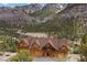 Beautiful log cabin home with a stone foundation is nestled among a forest of green trees, snowy mountains, and bright sky at 4927 Snow White Rd, Las Vegas, NV 89124